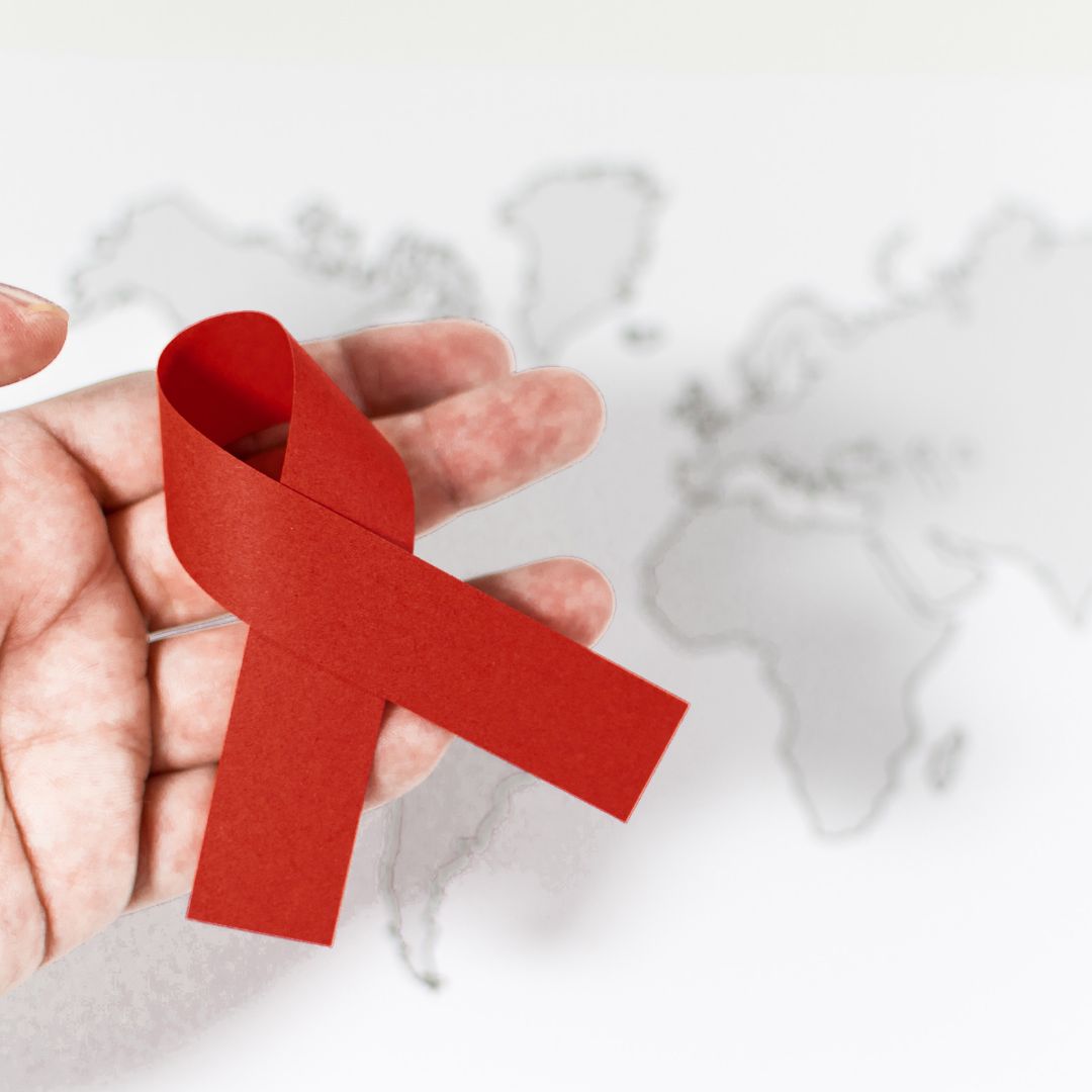 A red ribbon representative of World AIDS Day being held in the palm of a hand with a global map in the background