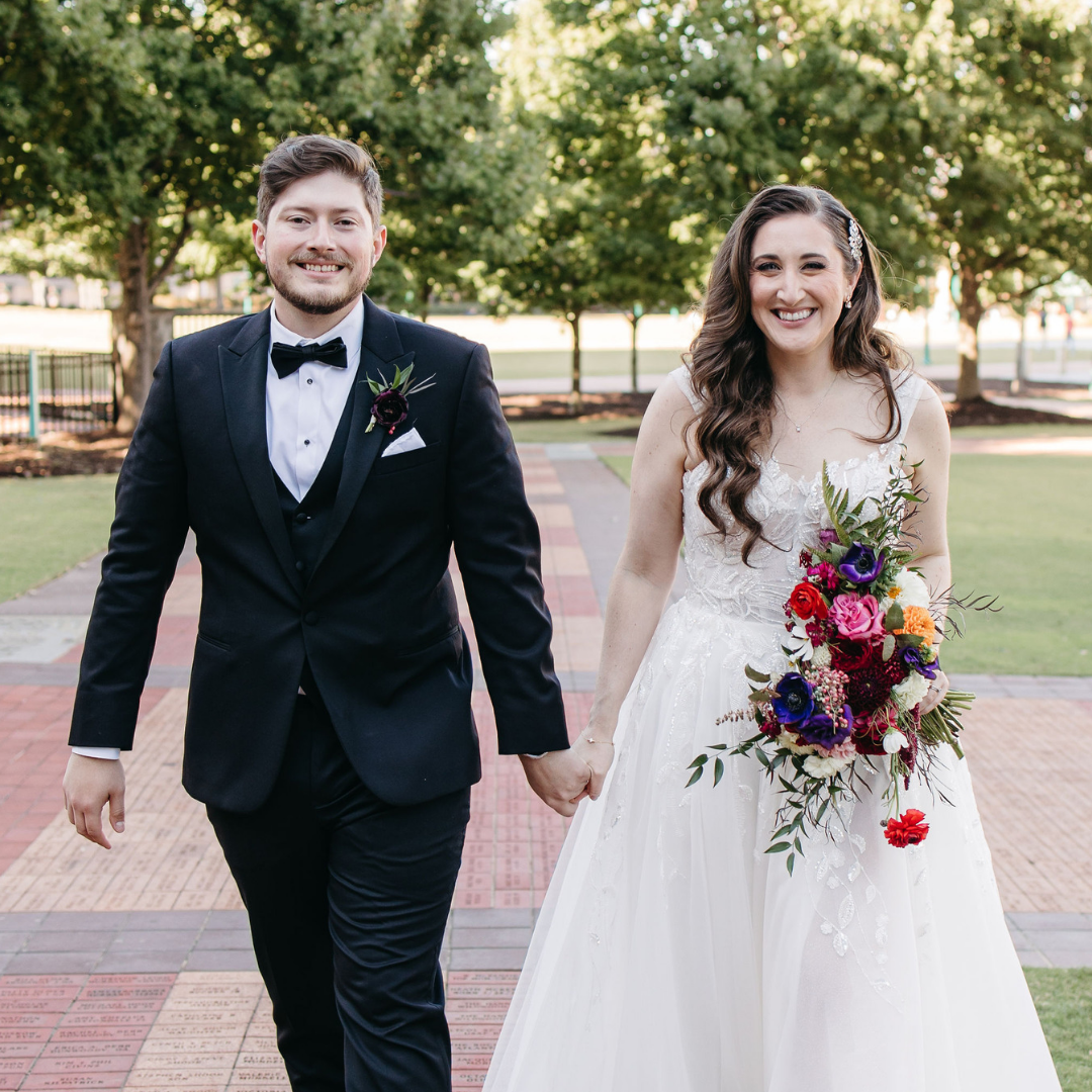 Wedding photo outdoors featuring the groom in a tuxedo and the bride in a white dress with a colorful bouquet